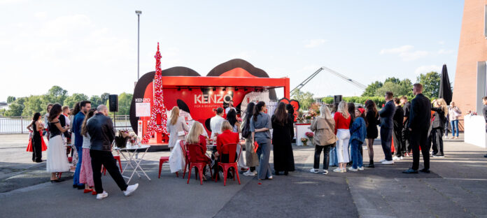 Mehrere Menschen vor einem in Rottönen gehaltenen Stand.